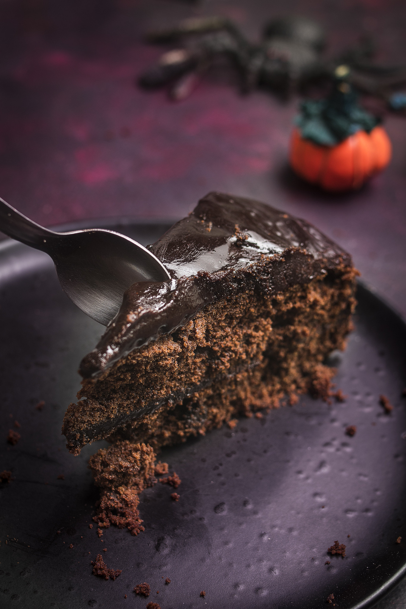 Slice of Chocolate Ghoulyard Cake with glossy espresso ganache and a spoon.
